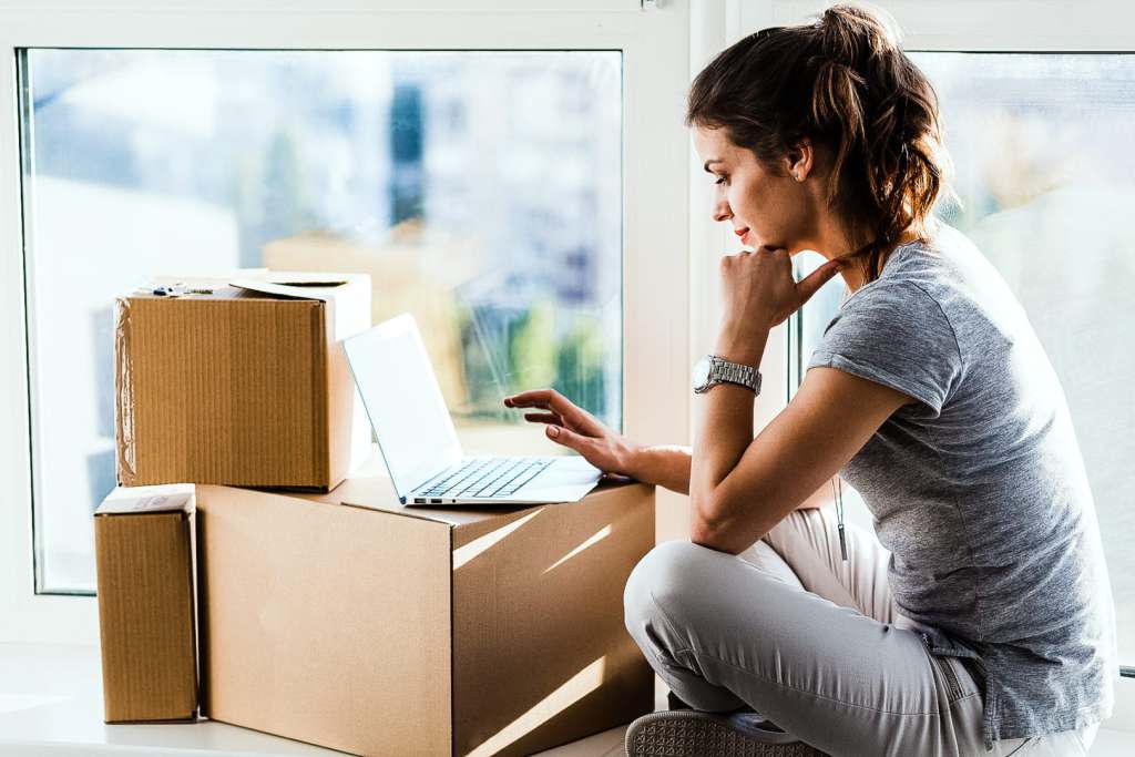 young travel nurse browsing the internet while surrounded by moving boxes
