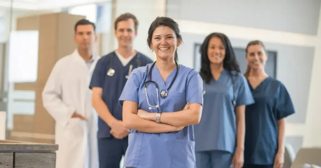 A group of healthcare professionals, including doctors and nurses, wearing medical scrubs and a lab coat, need to know the impacts for travel nurses from the 2026 Safe Staffing standards.