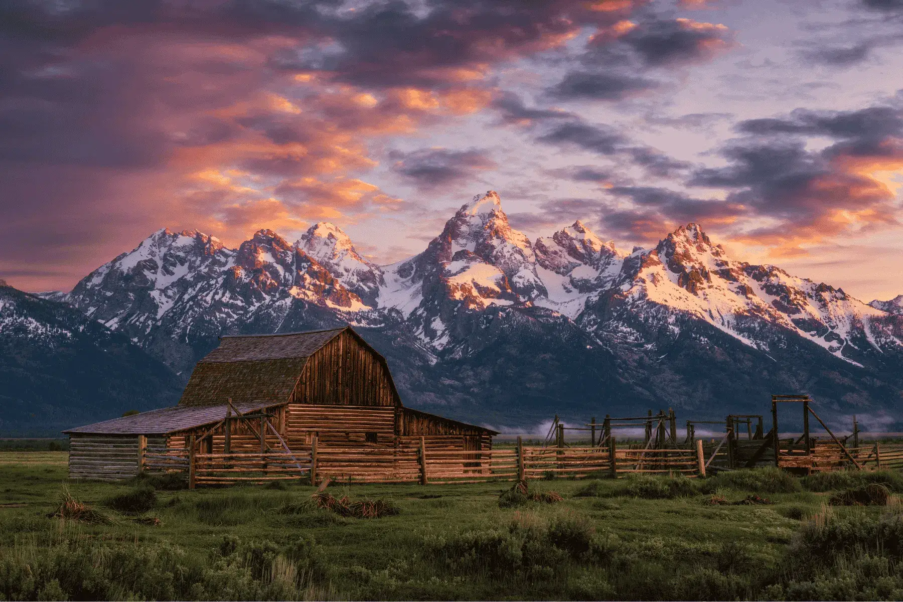 a picture of a barn with mountains in the background during sunset