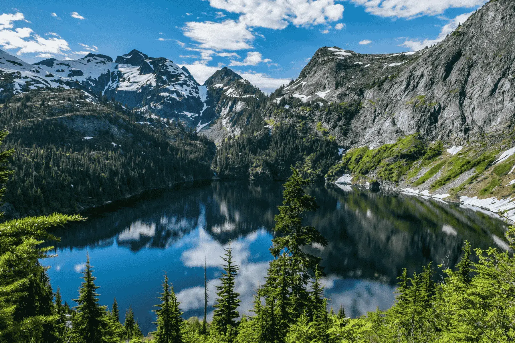 view of snowcapped mountains with a lake below surrounded by trees