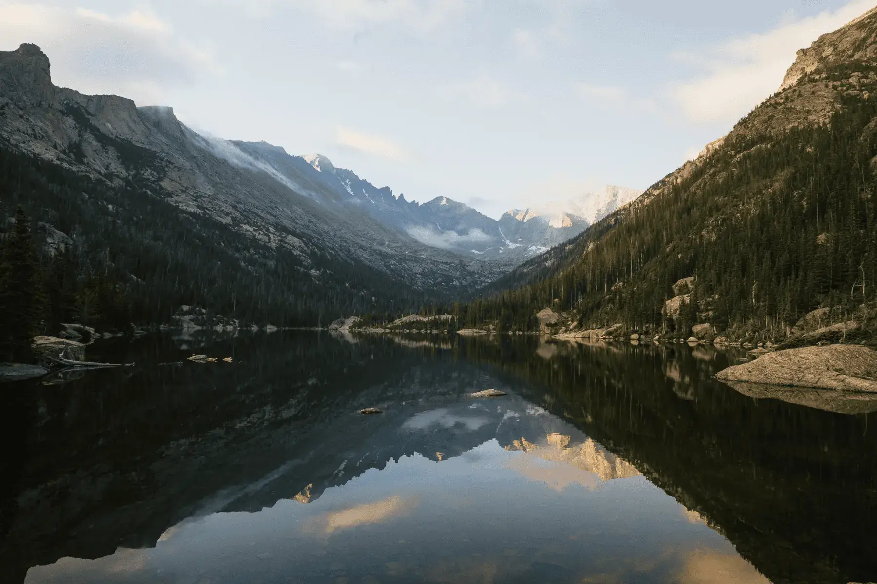 A picture of a mountain lake view surrounded by trees in the early morning