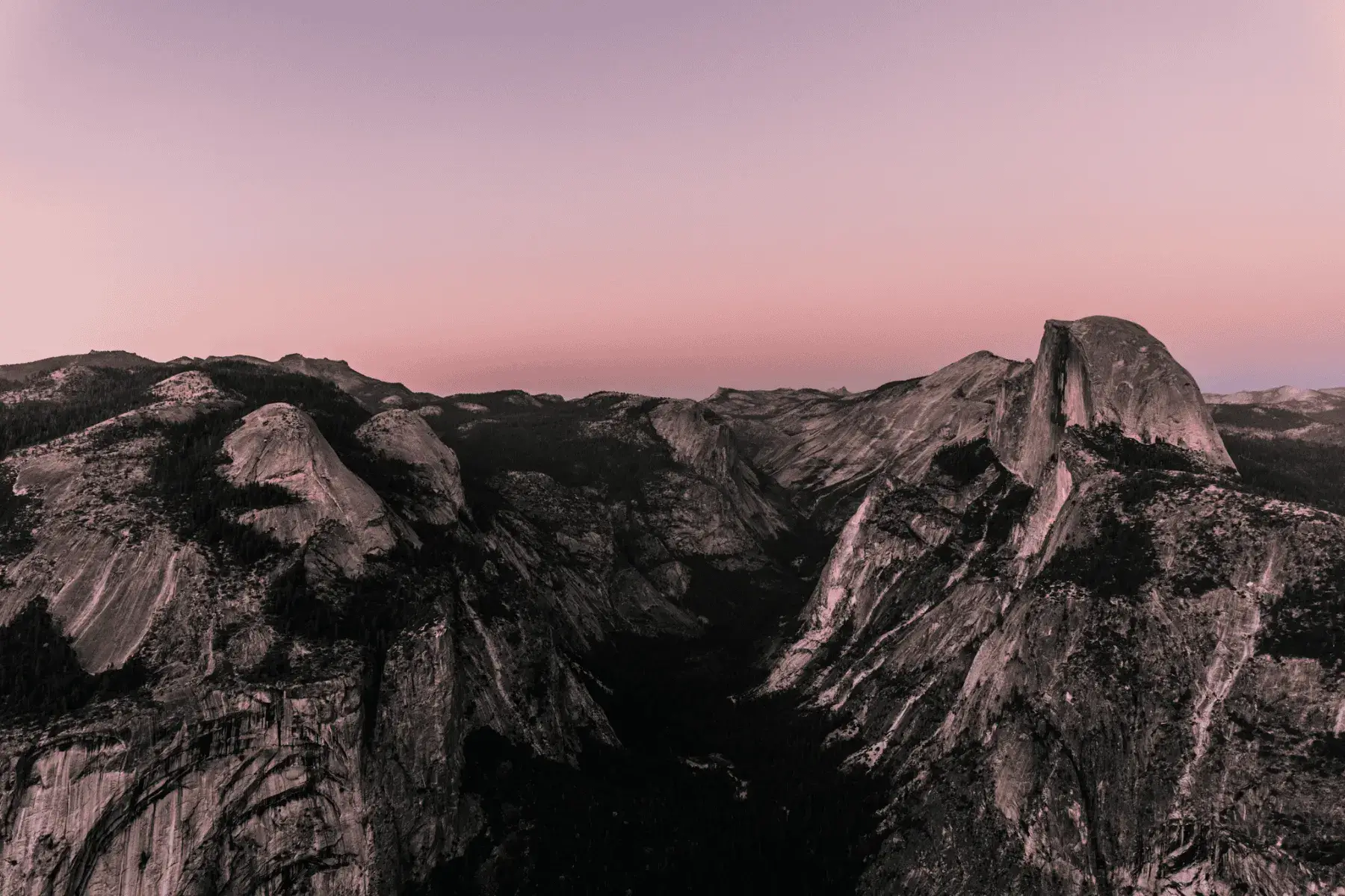 view of a mountainous valley during sunset with a pink glow