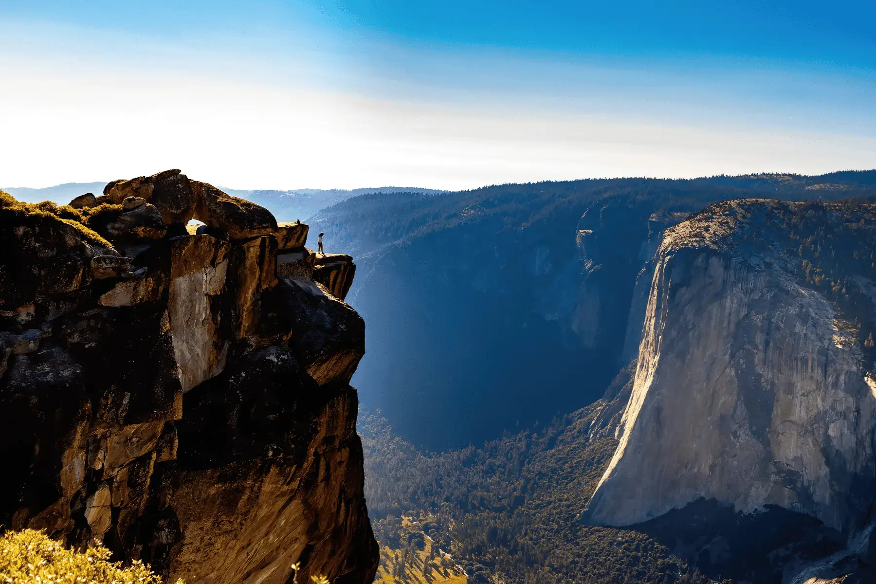 view of a woman standing on edge of mountain overlooking mountain valley
